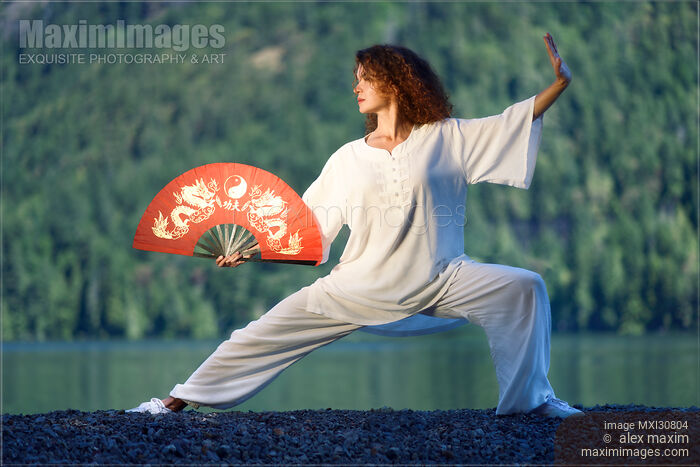 Stock photo of Woman with a red fan practicing Tai Chi Pu Bu stance at the lake shore in the nature Buy commercial use license at MaximImages