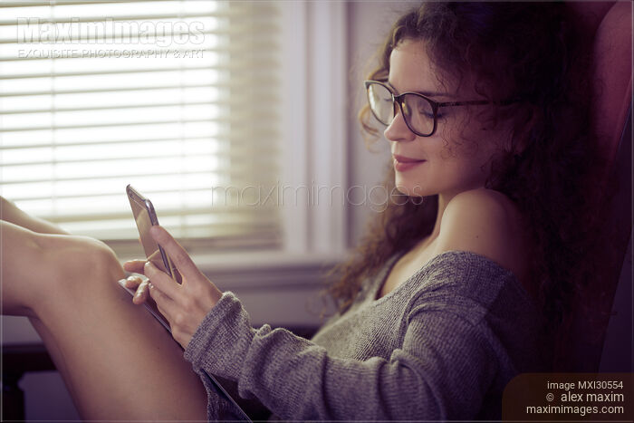 Woman with an iPhone in her hands sitting by the window texting Stock photo of Woman with an iPhone in her hands sitting by the window texting Buy commercial use license at MaximImages