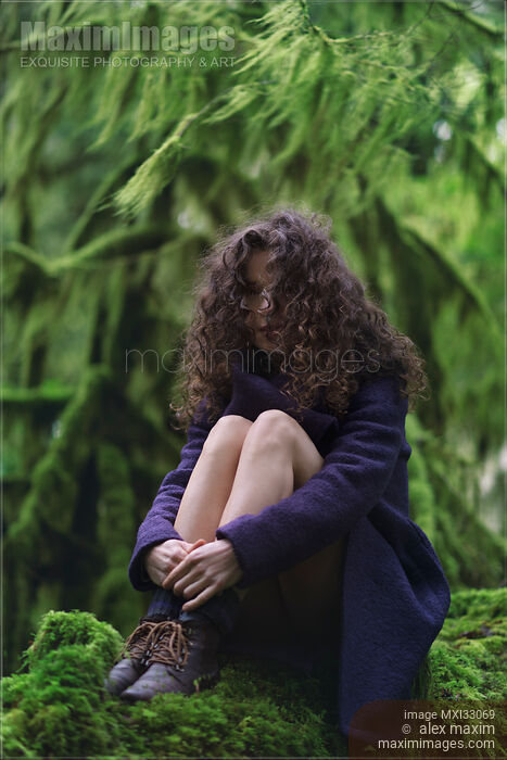 Woman with long curly hair and dreamy expression sitting in tranquil mossy green forest nature scenery Stock photo of Woman with long curly hair and dreamy expression sitting in tranquil mossy green forest nature scenery Buy commercial use license at MaximImages