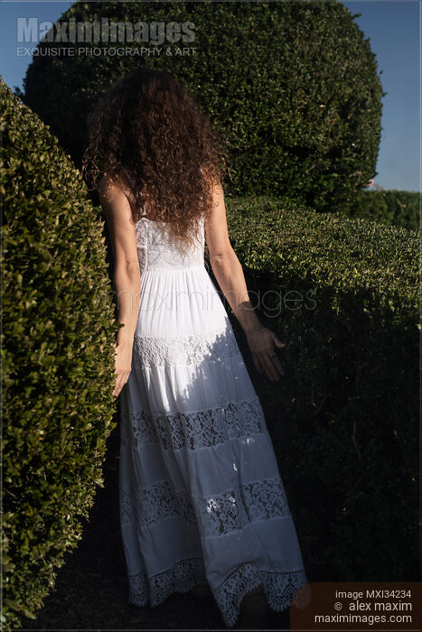 Young lady in white summer dress walking into a green garden disappearing behind the bushes Stock photo of Young lady in white summer dress walking into a green garden disappearing behind the bushes Buy commercial use license at MaximImages