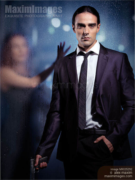 Young man in suit with a gun and woman behind glass Stock photo of Young man in suit with a gun and woman behind glass Buy commercial use license at MaximImages