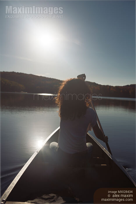 Stock photo of Young woman canoeing on a lake lin sunlight Buy commercial use license at MaximImages