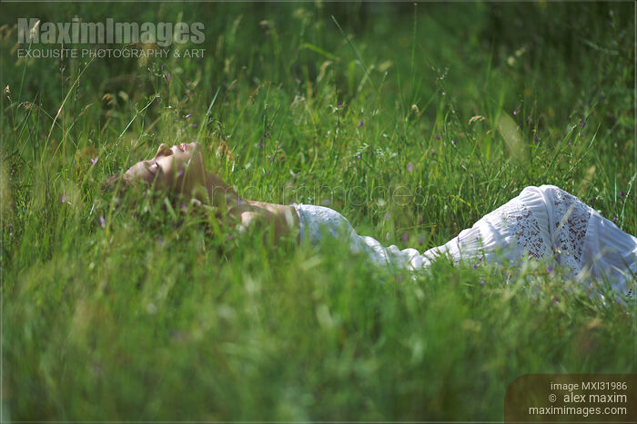 Young woman in a summer dress lying in green grassy field facing the sunlight in summer nature scenery Stock photo of Young woman in a summer dress lying in green grassy field facing the sunlight in summer nature scenery Buy commercial use license at MaximImages