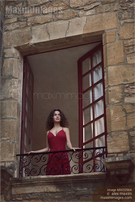 Young woman in red dress standing in an open balcony window of an old French house looking outside Stock photo of Young woman in red dress standing in an open balcony window of an old French house looking outside Buy commercial use license at MaximImages