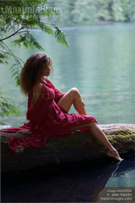 Stock photo of Young woman sitting on a tree in the nature with thoughtful expression dipping her foot in a lake Buy commercial use license at MaximImages