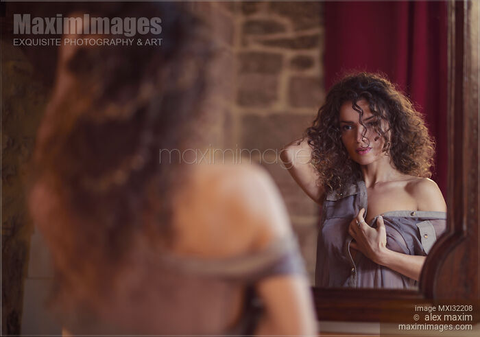 Stock photo of Young woman undressing in front of a mirror with a thoughtful look on her face Buy commercial use license at MaximImages
