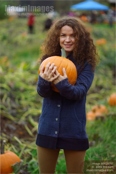 Stock photo of Young woman with a pumpkin at a farm in fall Buy commercial use license at MaximImages