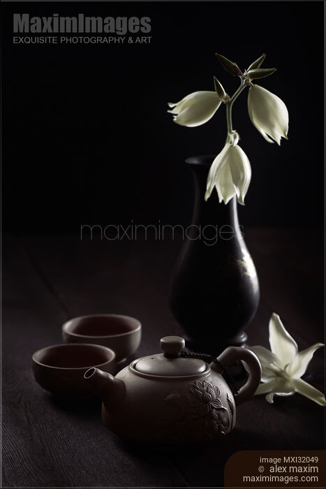 Zen still life of a clay teapot with tea cups and flowers in antique vase on black Stock photo of Zen still life of a clay teapot with tea cups and flowers in antique vase on black Buy commercial use license at MaximImages